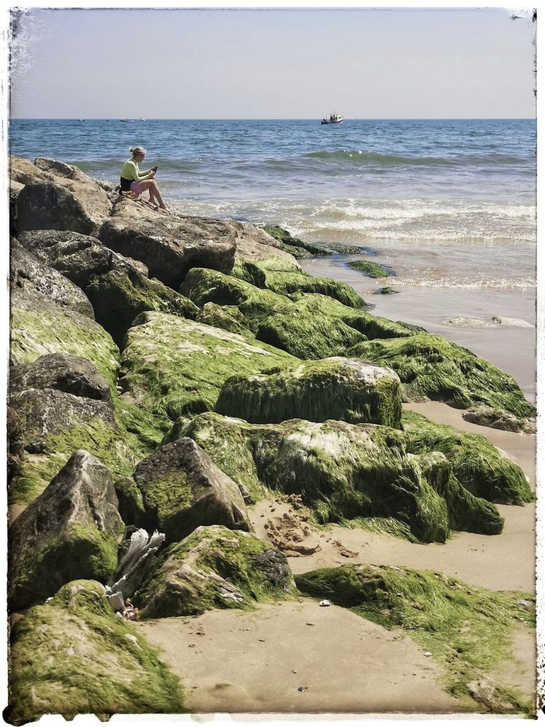 Seated figure overlooking the sea from a rocky shoreline